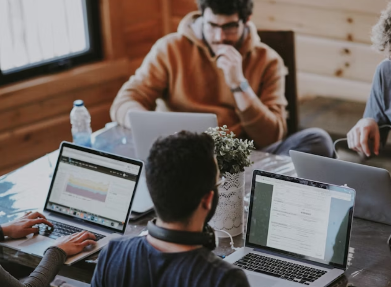 a group of people are sitting around a table using laptops